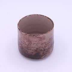 Close-up of a handmade Yunomi cup showing the irregular iron oxide and terra rosa surface with visible grog texture