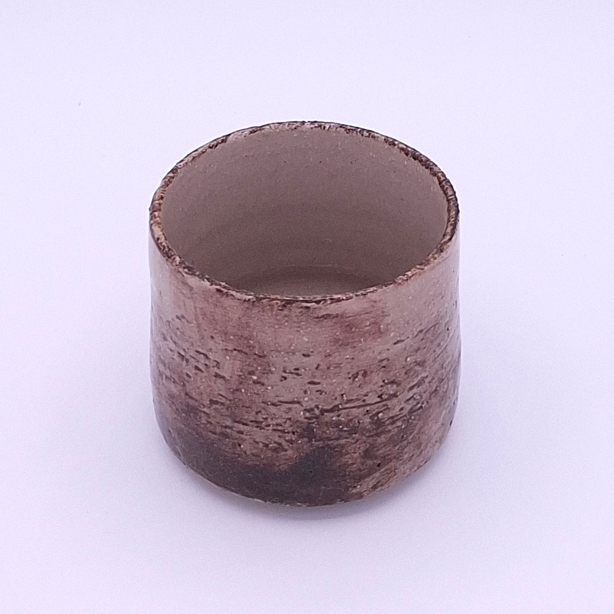 Close-up of a handmade Yunomi cup showing the irregular iron oxide and terra rosa surface with visible grog texture