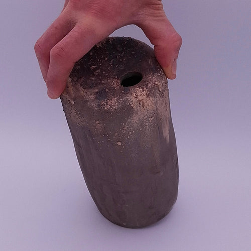 Handmade anthracite stoneware Rubble Vase II held in one hand, showing its dark iron oxide surface, textured rim and small opening.
