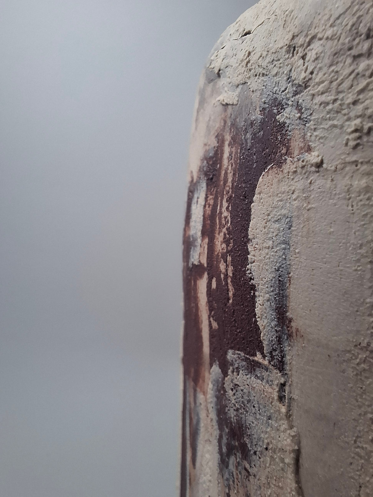 Close-up of Rubble Vase I showing the textured cream stoneware surface and irregular rust-coloured marks created with natural mineral pigment from Portugal.