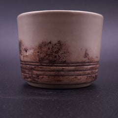 Close-up of a handmade 200 ml Yunomi cup showing its cream stoneware interior and irregular dark iron oxide pattern around the lower exterior.