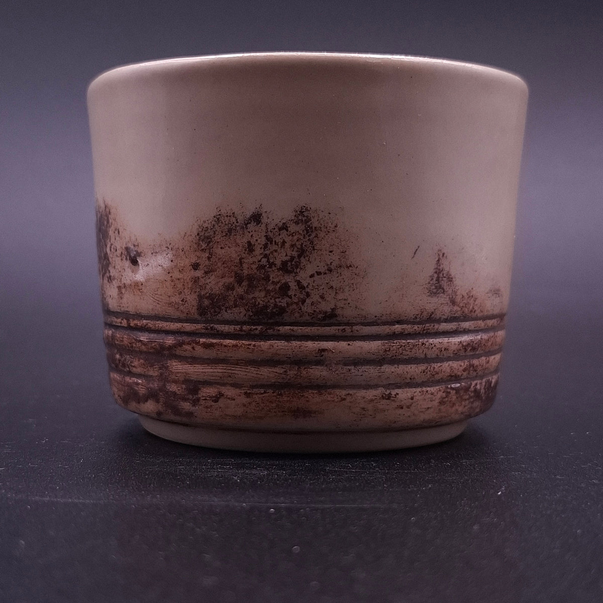 Close-up of a handmade 200 ml Yunomi cup showing its cream stoneware interior and irregular dark iron oxide pattern around the lower exterior.